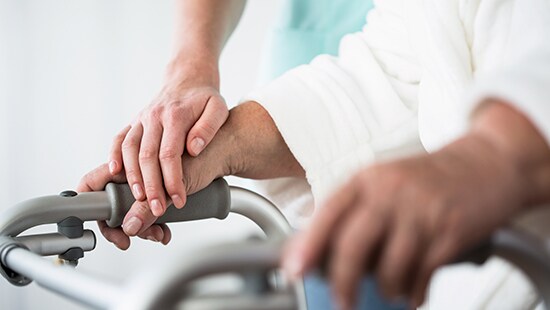 Close up of elderly hands holding walker with hands of healthcare provider helping.