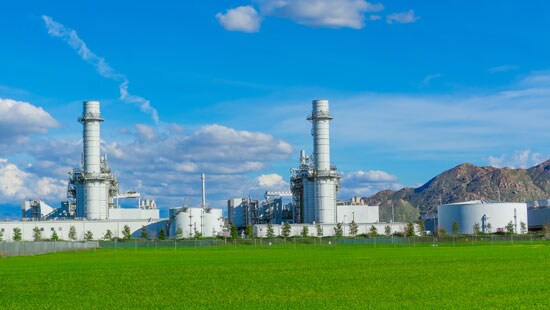 Massive gas fired power plant near a long mountain range on a sunny day.