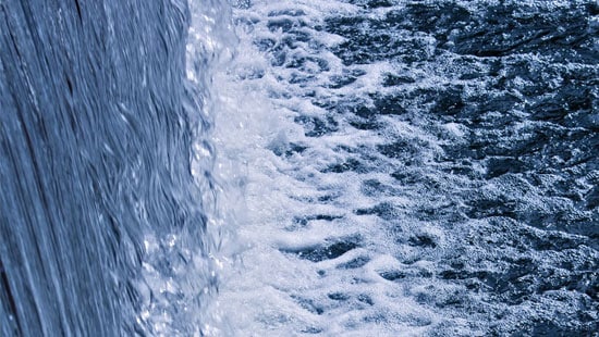 Shoreline view of a freshwater waterfall crashing onto a lake. 