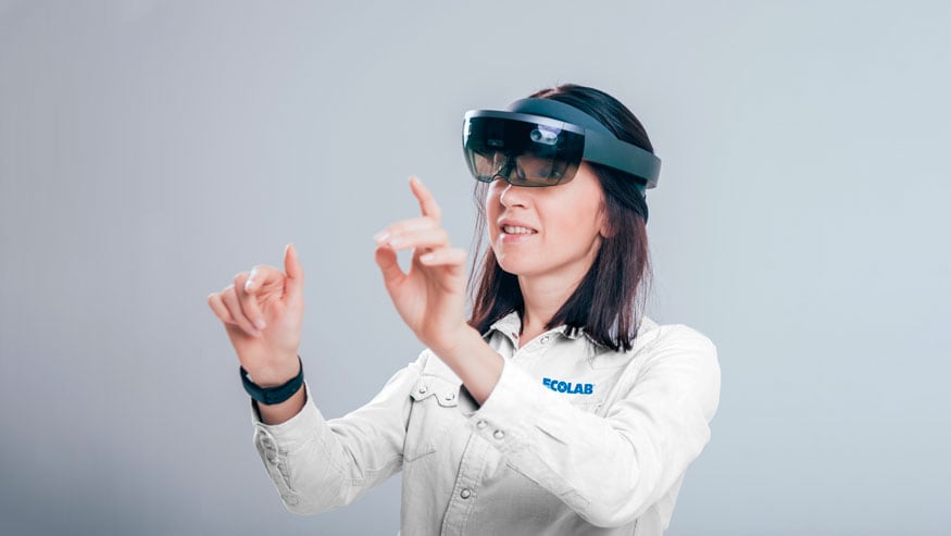 Worker in an Ecolab jacket wearing the Microsoft HoloLens 2 device and gesturing with their hands.